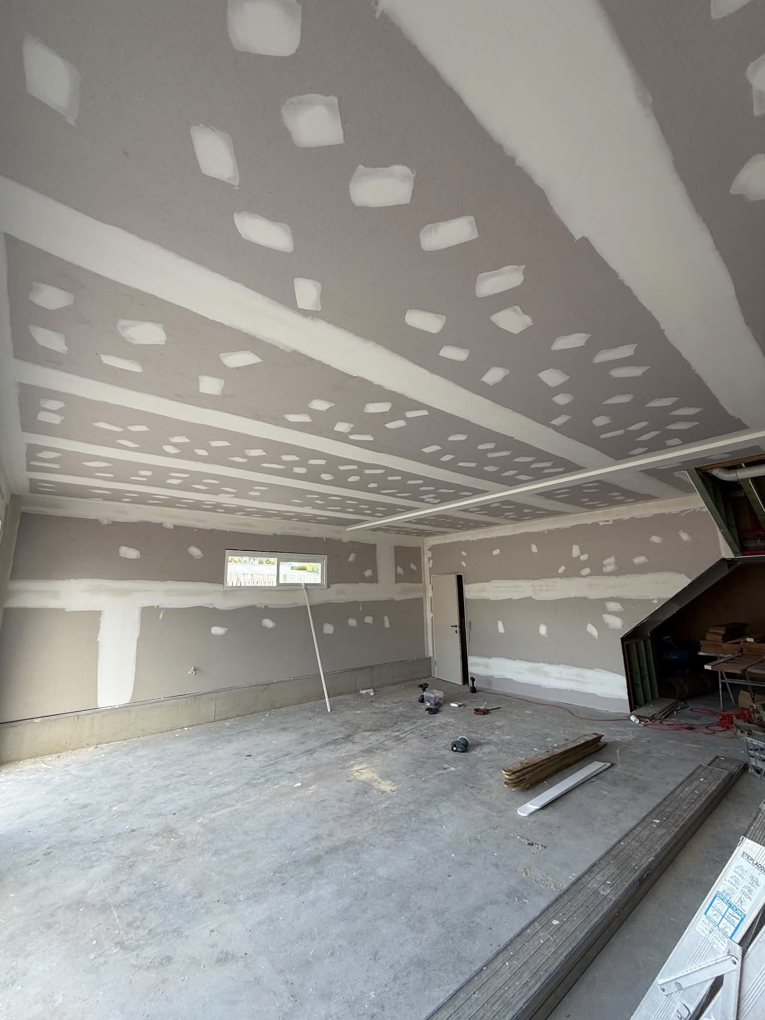 Room with fresh plasterboard being mudded and taped across the ceiling