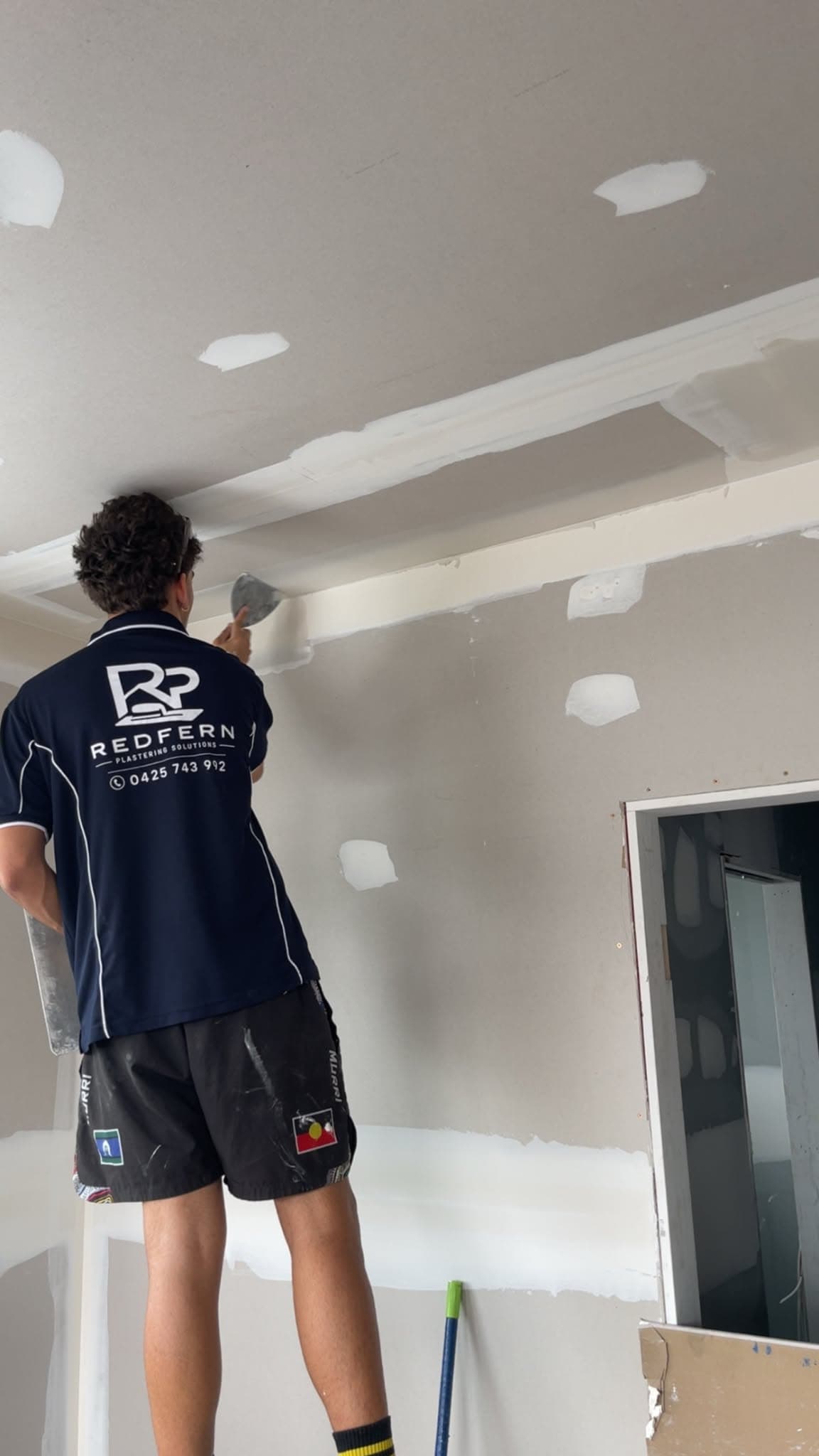Redfern plasterer in branded polo taping the wall-to-ceiling junction during a renovation