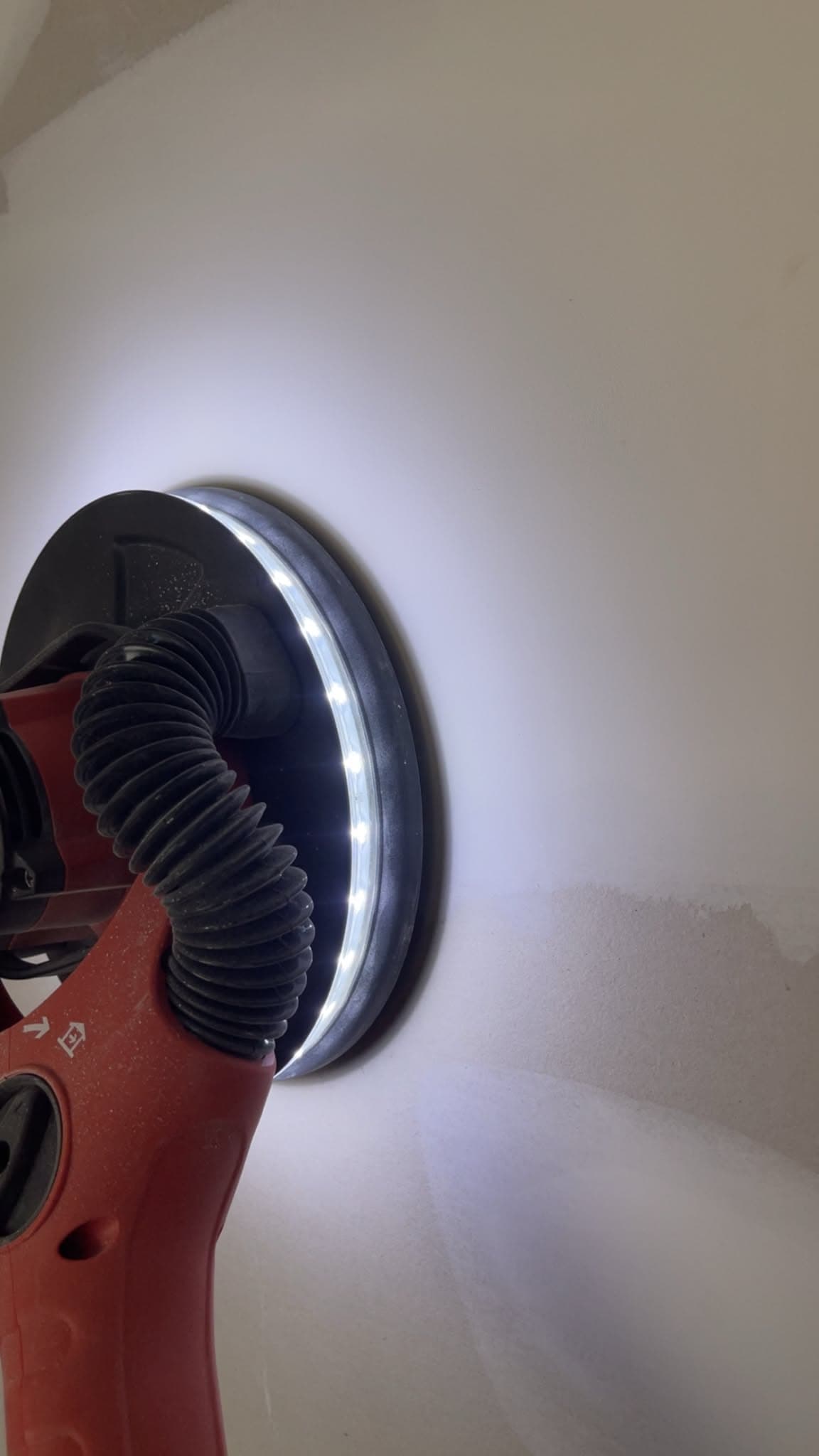 Power sander with LED ring light and dust extraction smoothing a wall before paint